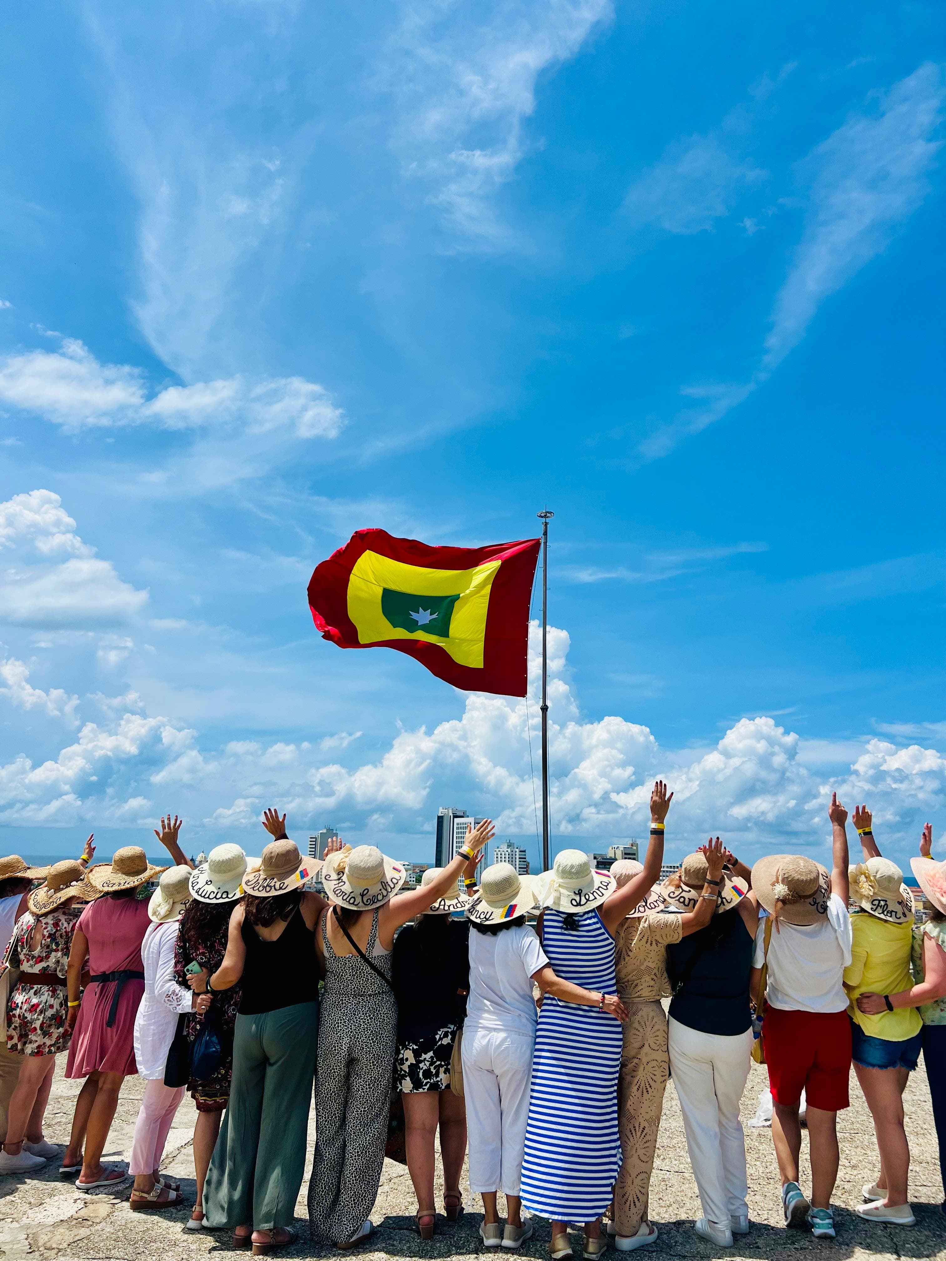 Andariegas de espaldas con sombreros levantando las manos frente a la bandera de Cartagena