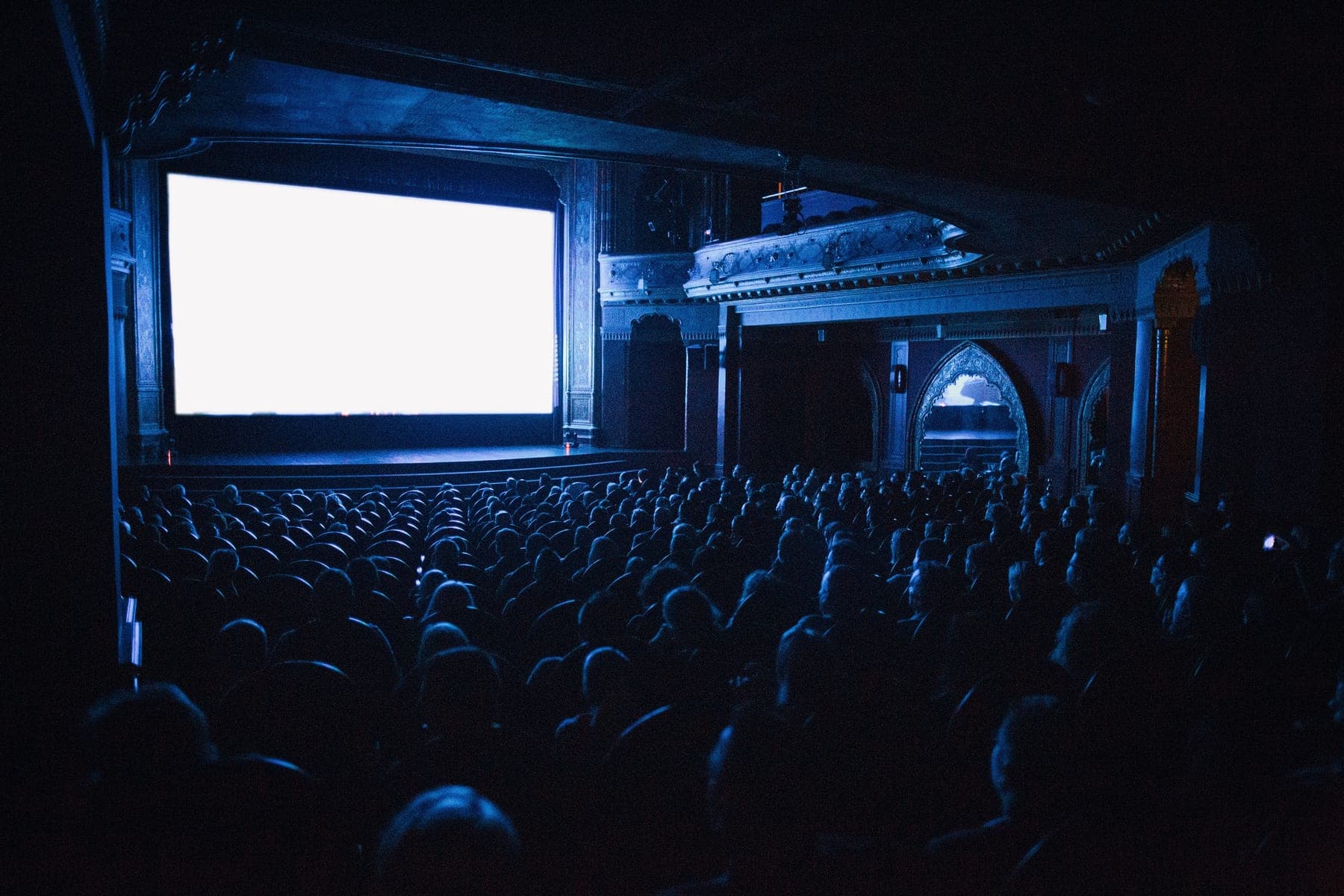 Sala de teatro a oscuras con el público sentado frente al escenario iluminado
